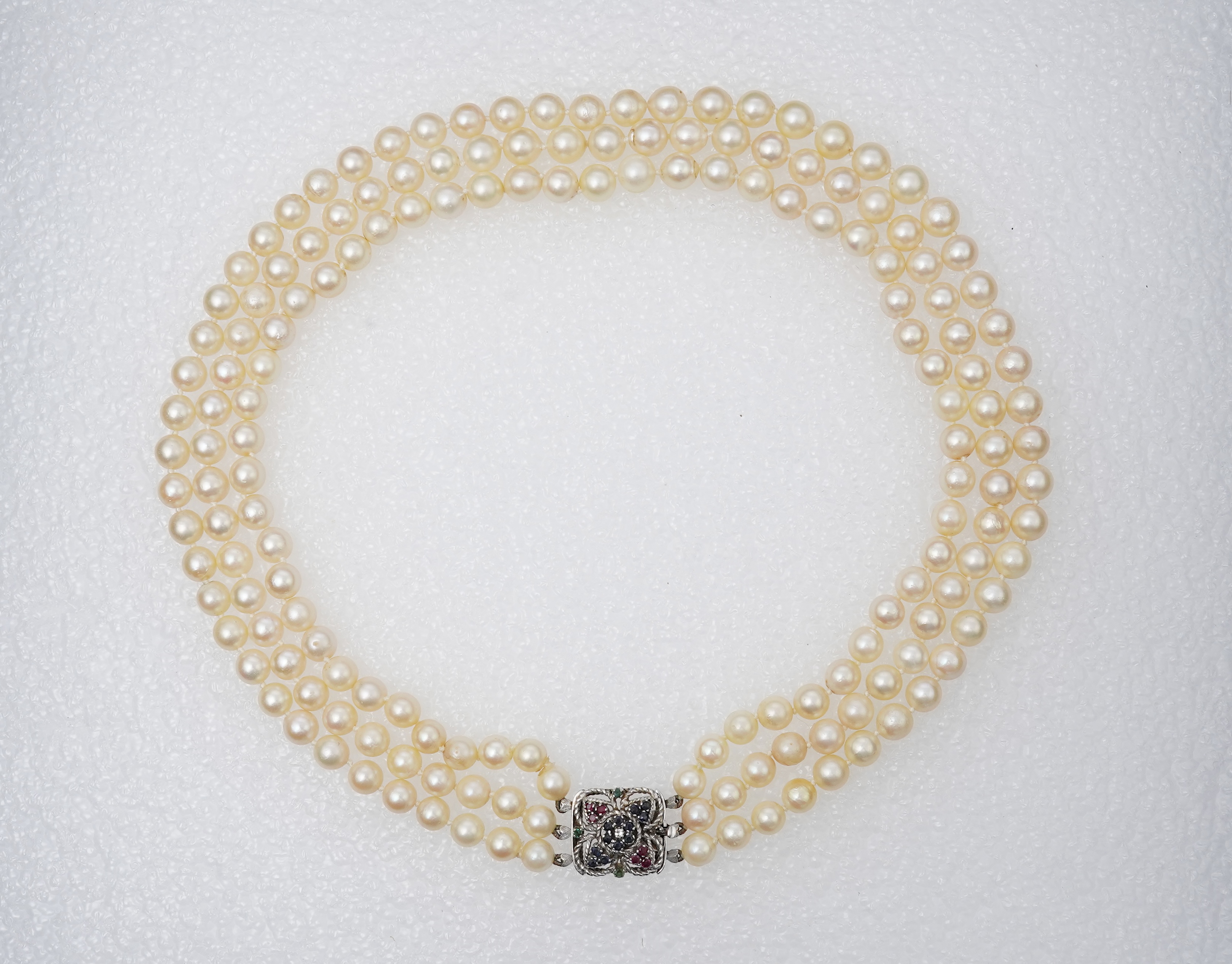 A mid to late 20th century Italian triple strand cultured pearl necklace, with emerald, sapphire and ruby cluster set 750 white metal clasp, 44cm.